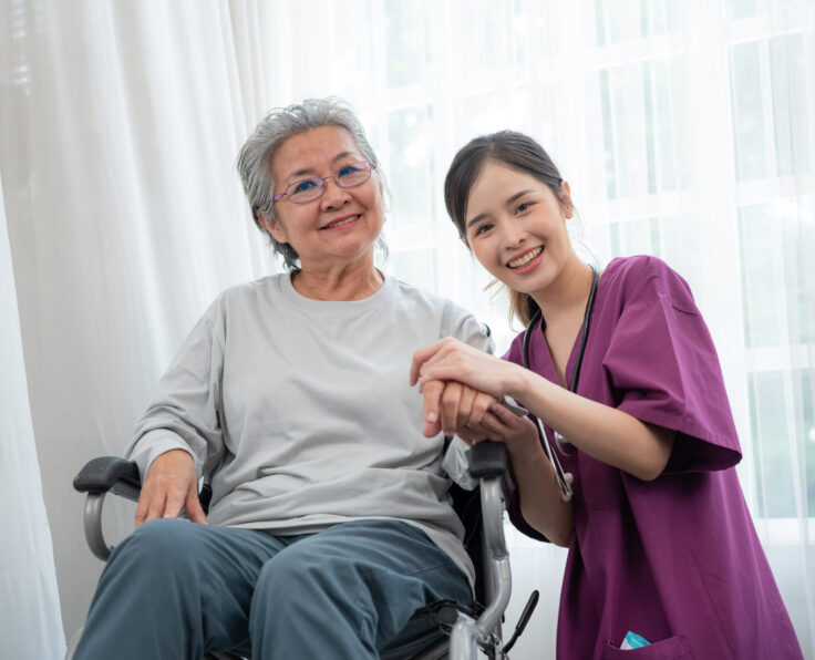 Asian young nurse taking care and talking mature female patient sitting on wheelchair in hospital. Healthcare concept.