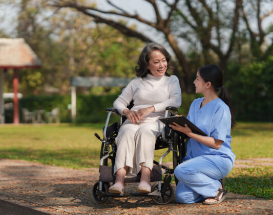 Elderly asian senior woman on wheelchair with nurse. Nursing home hospital garden concept.